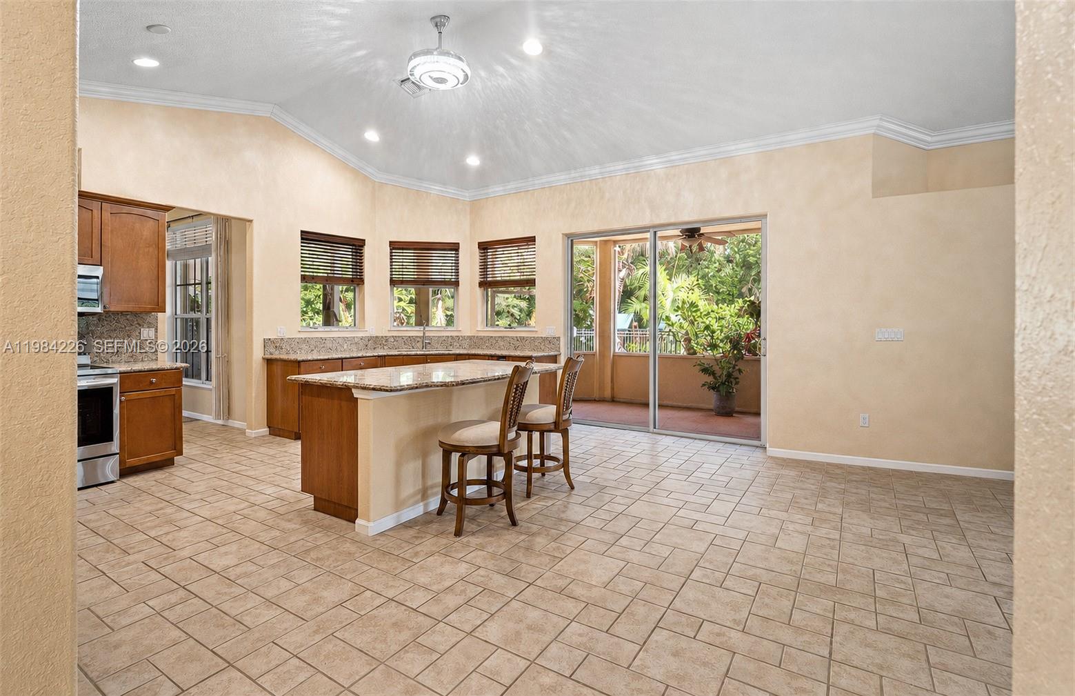 A kitchen with wood cabinets, granite countertops, an island with bar stools, and sliding doors — 5026 Coconut Blvd, Palm Beach FL 33411, PALM BEACH, FL