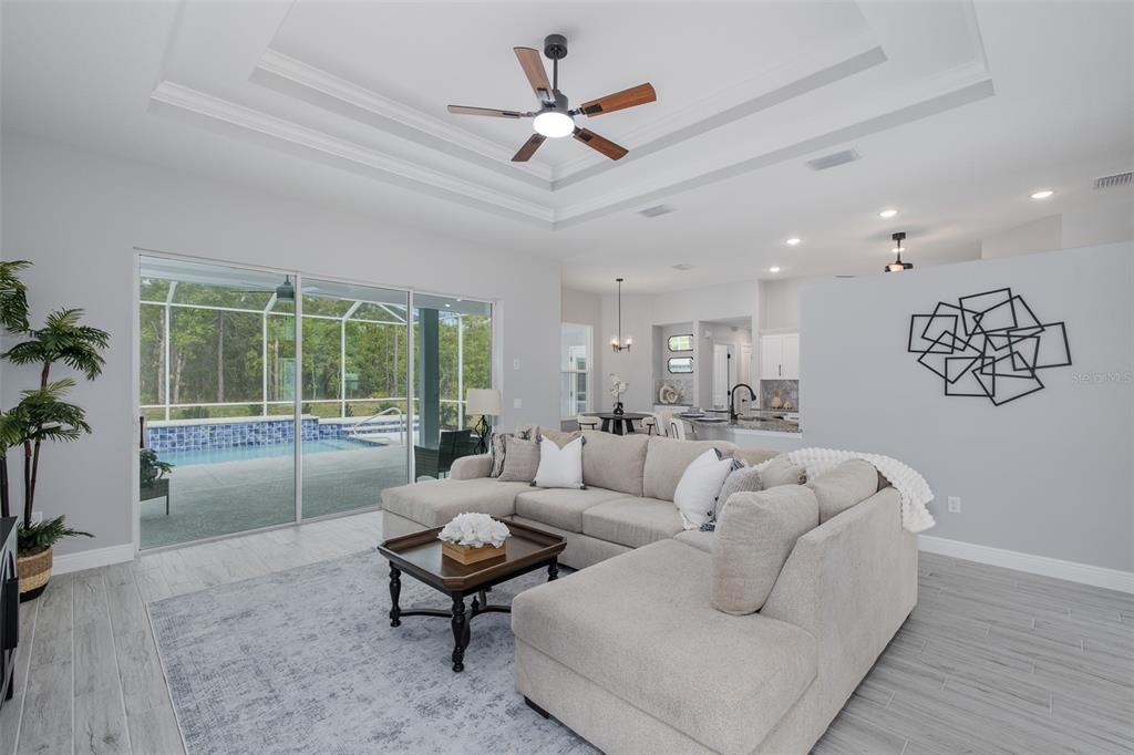 A living room with a sectional sofa, tray ceiling, and sliding doors opening to a pool — 38 VINCA STREET, HOMOSASSA, FL