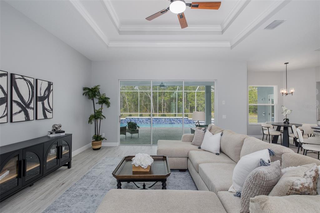 A living room with a sectional sofa, tray ceiling, and sliding doors opening to a pool — 38 VINCA STREET, HOMOSASSA, FL