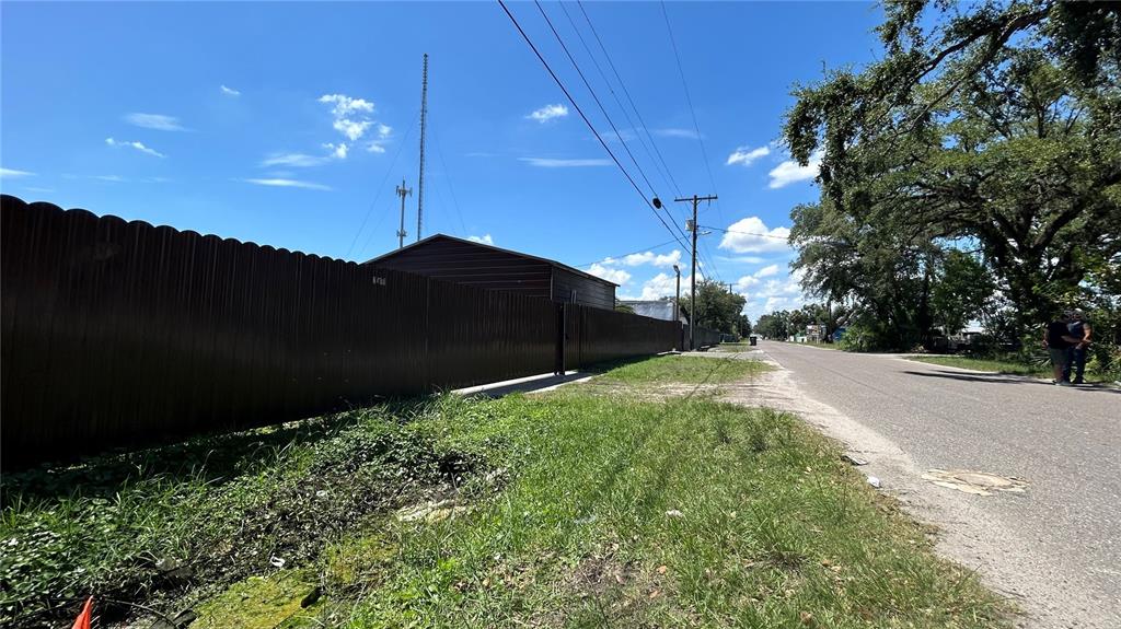 A brown metal fence runs along a grassy roadside next to a building and utility poles — 2001 S 51ST STREET, TAMPA, FL