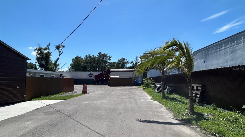 An outdoor paved lot sits between two fenced areas with a palm tree and buildings — 2001 S 51ST STREET, TAMPA, FL