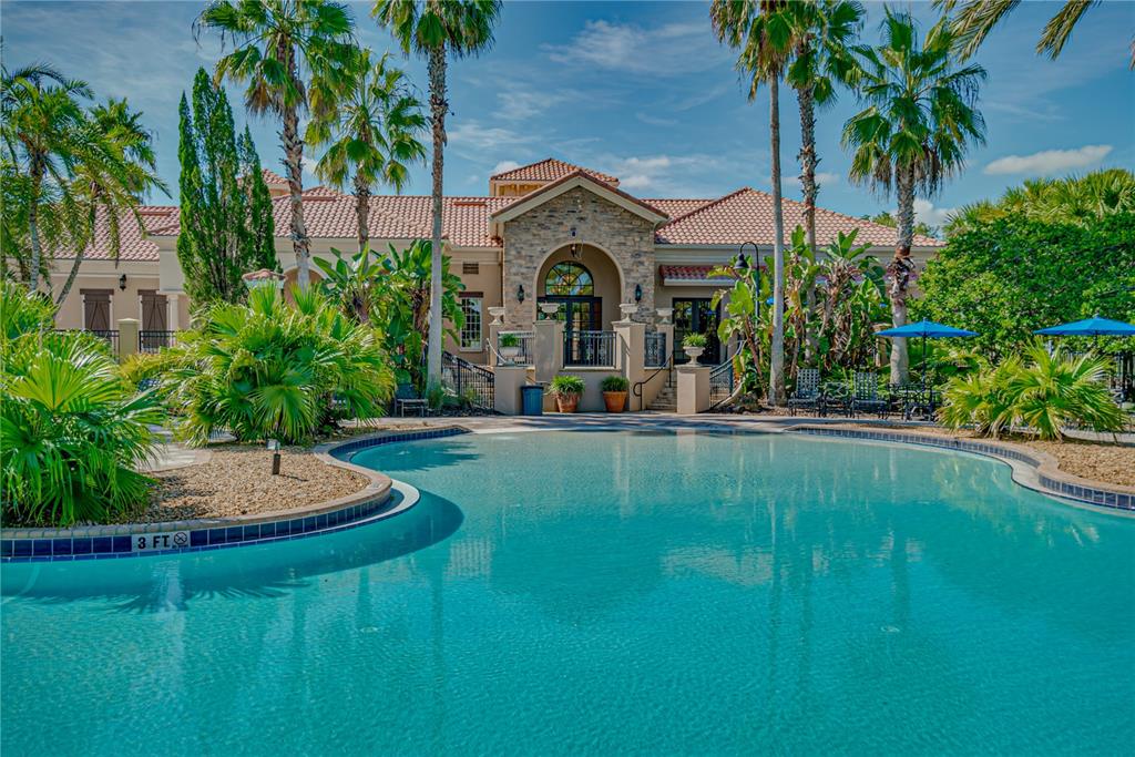 A swimming pool sits in front of a Mediterranean-style building with palm trees and landscaping — 1894 VIA LAGO DRIVE, LAKELAND, FL