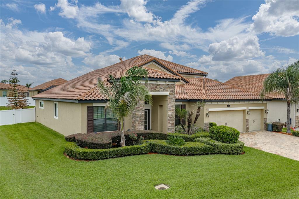 A single-story house with a tile roof, stone facade, and manicured landscaping under a cloudy sky — 1894 VIA LAGO DRIVE, LAKELAND, FL