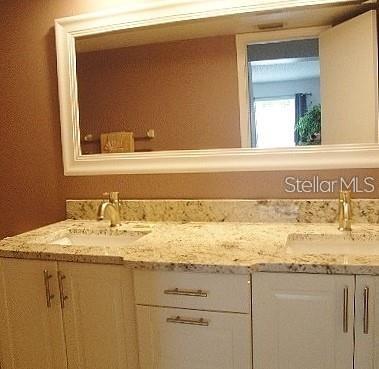 A bathroom vanity features a granite countertop, dual sinks, white cabinets, and a large mirror — 6061 BAHIA DEL MAR BOULEVARD UNIT 110, ST PETERSBURG, FL