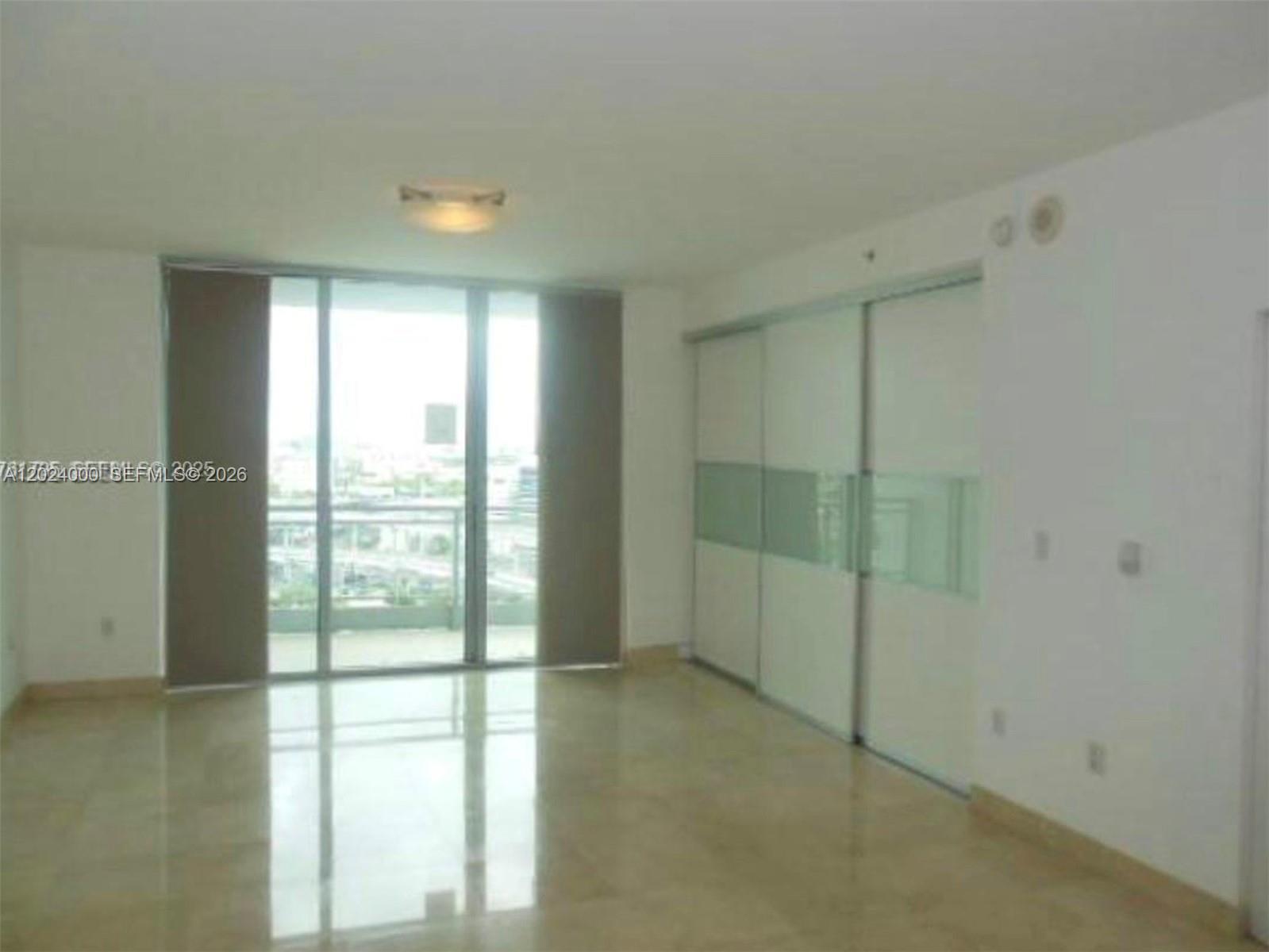 An empty room features light-colored tile flooring, white walls, and a large sliding glass door — 90 SW 3rd St # 1811, Miami FL 33130, MIAMI, FL