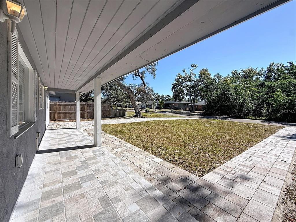 A covered patio with light-colored pavers overlooks a grassy yard and a residential street — 1408 ROGERS STREET, CLEARWATER, FL