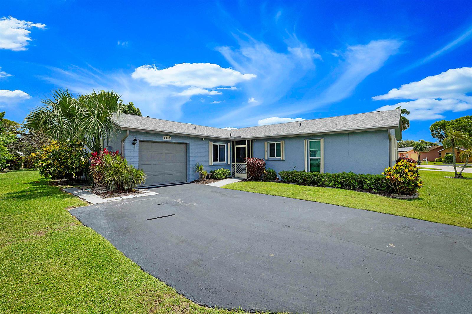 A single-story blue house with a garage, driveway, and lawn under a blue sky — 6309 Summer Sky Lane, FL 33463, FL