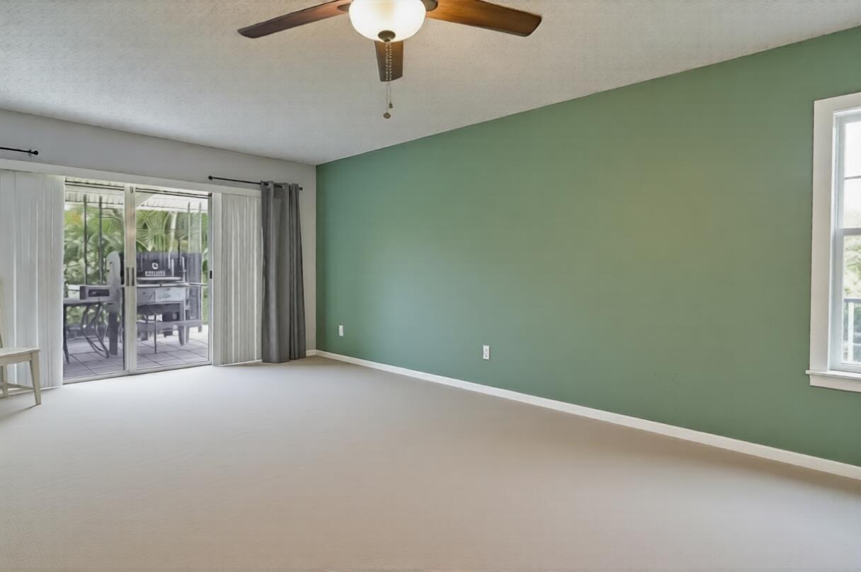 An empty room features a green accent wall, beige carpeting, and a sliding glass door — 6309 Summer Sky Lane, FL 33463, FL