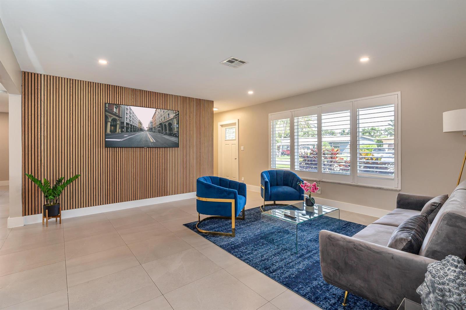 A living room features a wood-slat accent wall, blue armchairs, a gray sofa, and tile flooring — 300 SE 8th Court, Pompano Beach FL 33060, POMPANO BEACH, FL