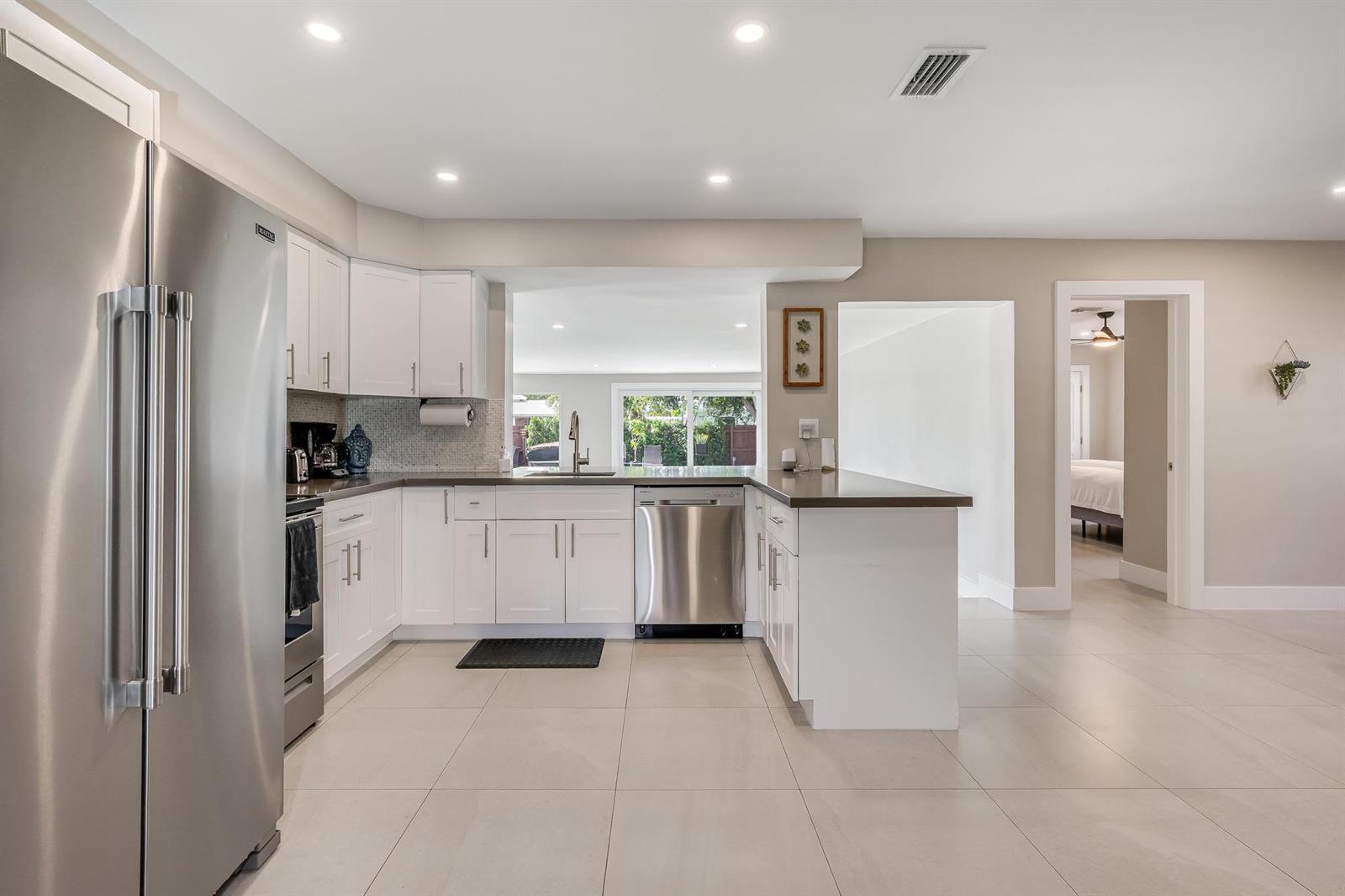 A modern kitchen features white cabinets, stainless steel appliances, and light tile flooring — 300 SE 8th Court, Pompano Beach FL 33060, POMPANO BEACH, FL