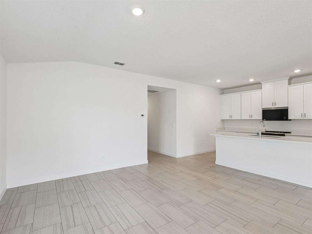 A modern kitchen with white cabinets, quartz countertops, and a large island overlooks an open space — 20 GARNI DRIVE, PALM COAST, FL