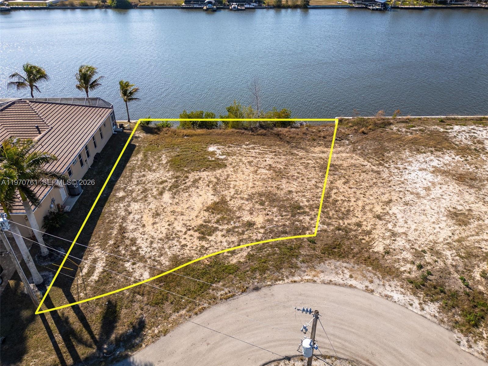 An aerial view shows a vacant waterfront lot outlined in yellow next to a house — 2826 NW 43rd, Cape Coral FL 33993, CAPE CORAL, FL
