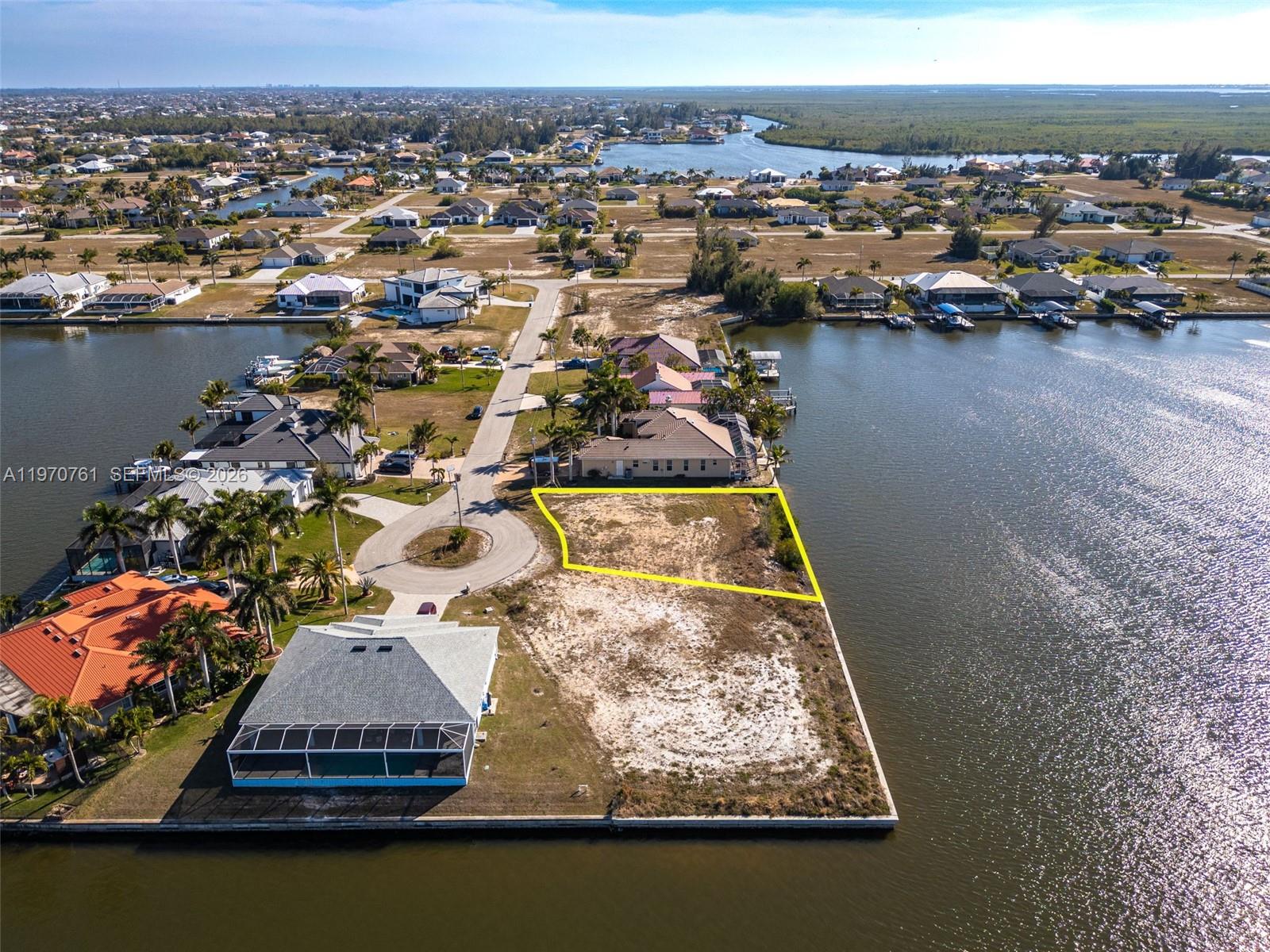 An aerial view shows a vacant waterfront lot outlined in yellow next to a residential street — 2826 NW 43rd, Cape Coral FL 33993, CAPE CORAL, FL