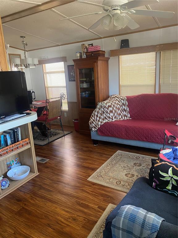 A living room with wood-look flooring, a red sofa, a dining area, and a ceiling fan — 4812 ELWANA WAY, ZEPHYRHILLS, FL