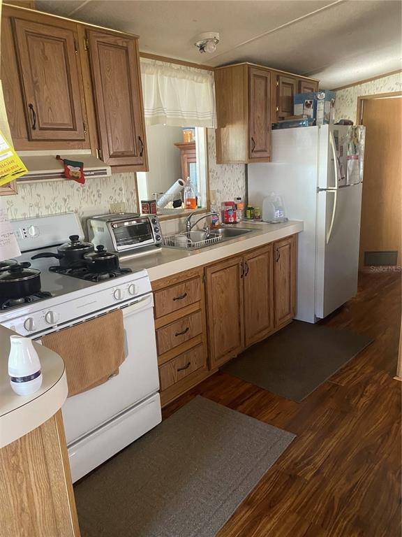 A kitchen features wood cabinets, white appliances, laminate countertops, and wood-look flooring — 4812 ELWANA WAY, ZEPHYRHILLS, FL