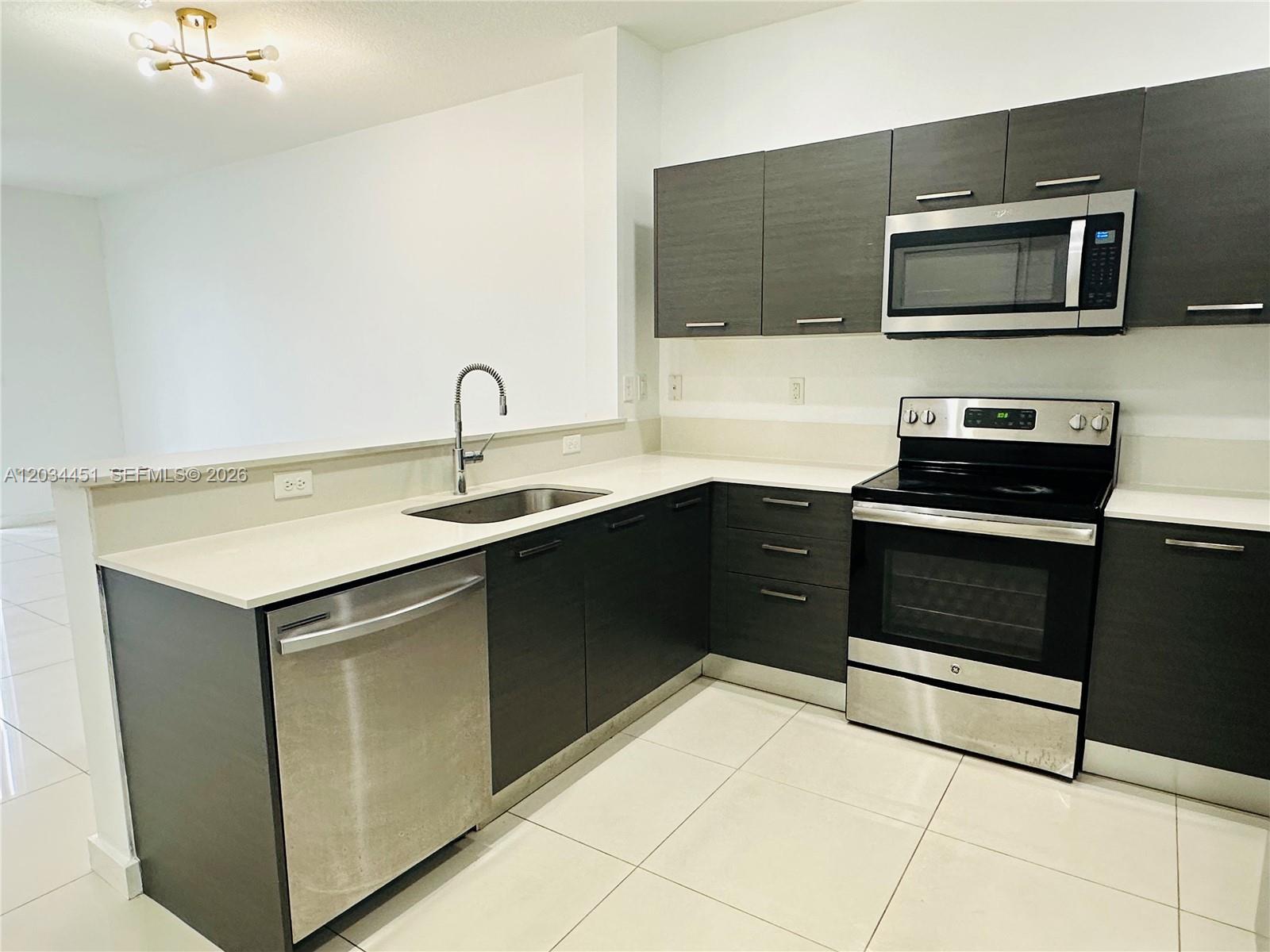 A modern kitchen features dark wood cabinets, stainless steel appliances, and white countertops — 3507 NW 13th St, Lauderhill FL 33311, LAUDERHILL, FL