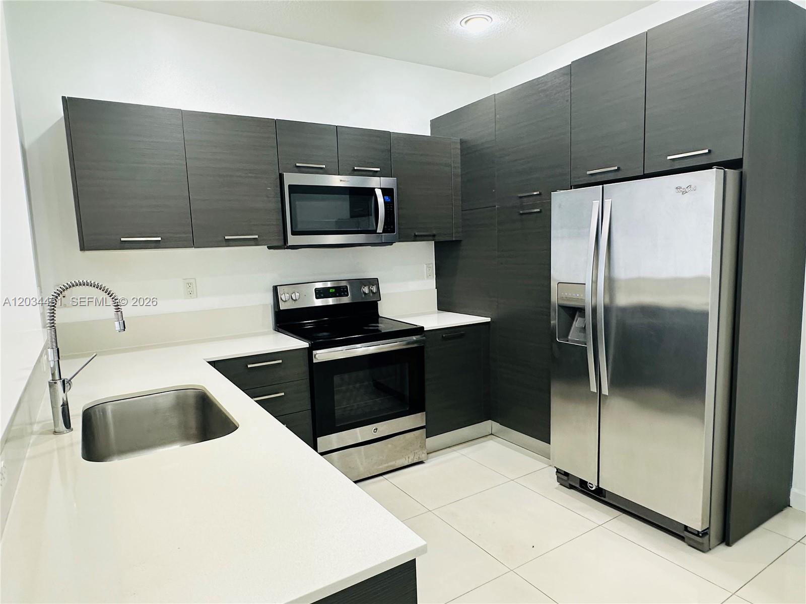 A modern kitchen features dark wood cabinets, stainless steel appliances, and white quartz countertops — 3507 NW 13th St, Lauderhill FL 33311, LAUDERHILL, FL