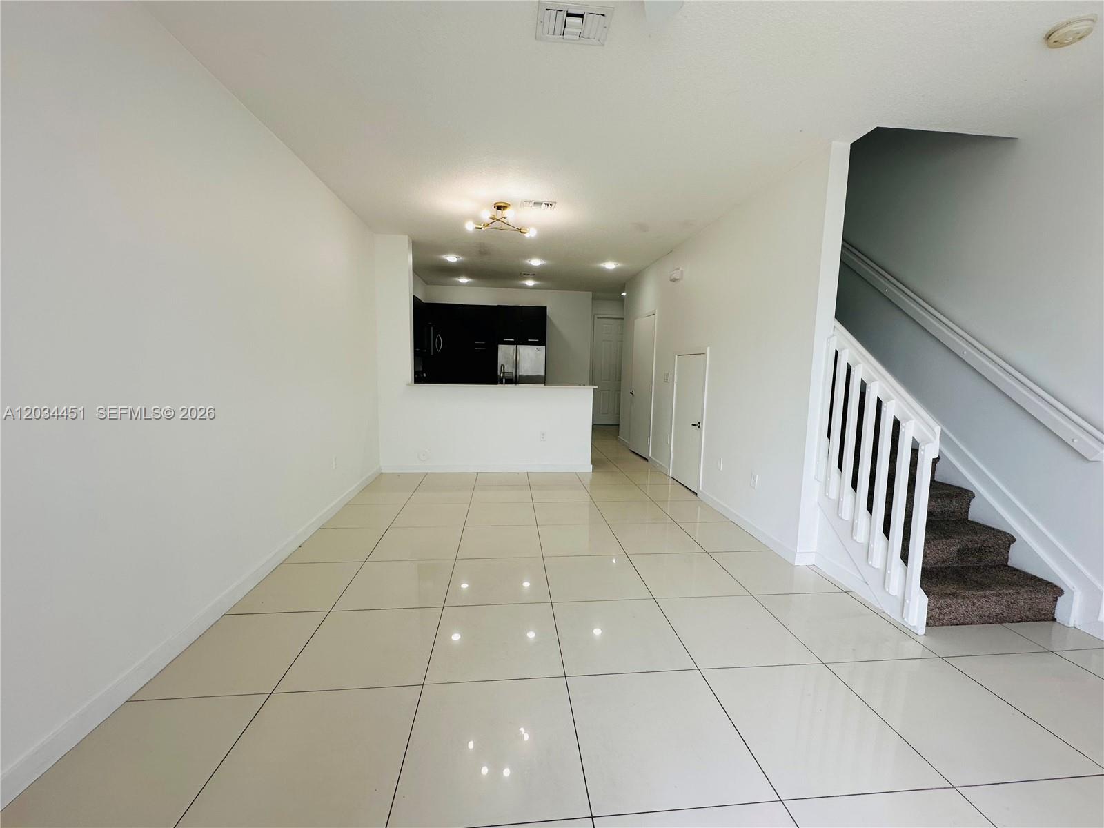 An open-concept living area features white tile flooring, a kitchen with dark cabinets, and stairs — 3507 NW 13th St, Lauderhill FL 33311, LAUDERHILL, FL