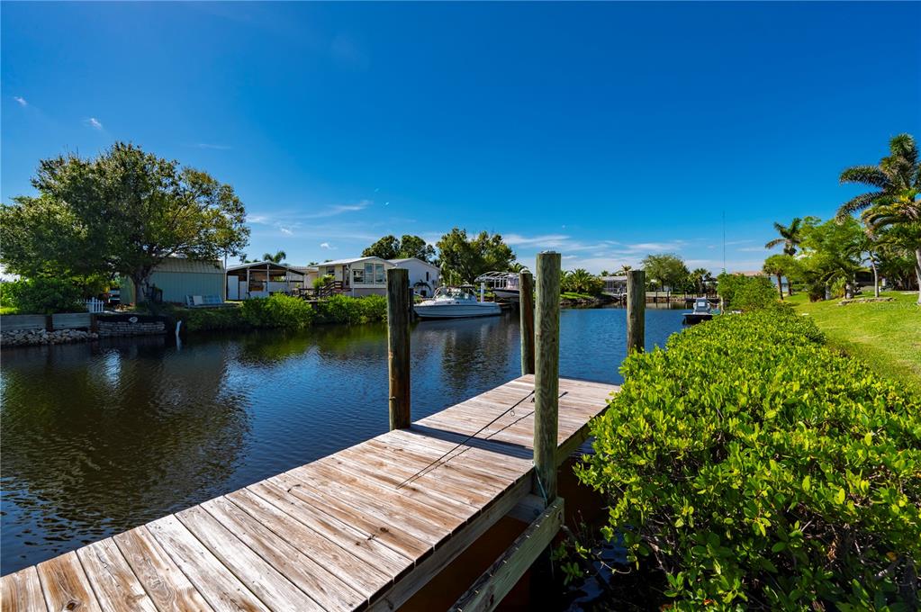 A wooden dock extends into a canal lined with mangroves, boats, and waterfront homes — 4220 DELTONA DRIVE, PUNTA GORDA, FL