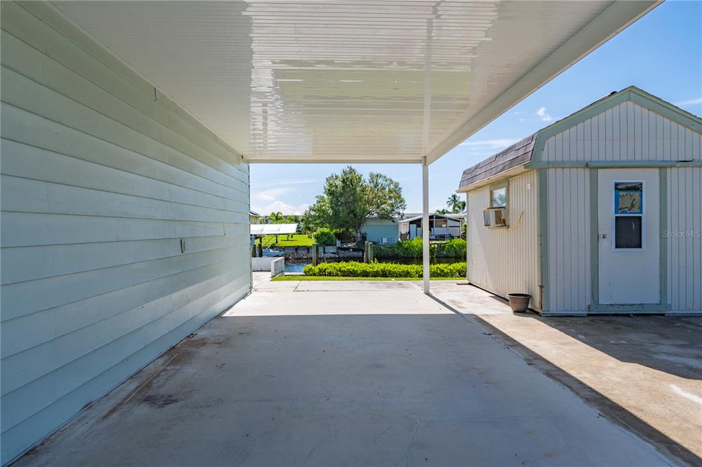 A concrete carport sits beside a small shed with a view of a canal — 4220 DELTONA DRIVE, PUNTA GORDA, FL