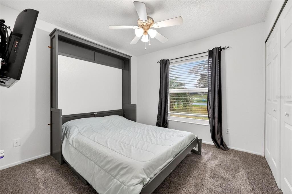 A bedroom features a gray Murphy bed, a ceiling fan, and a window with curtains — 5107 DEER CREEK DRIVE, ORLANDO, FL