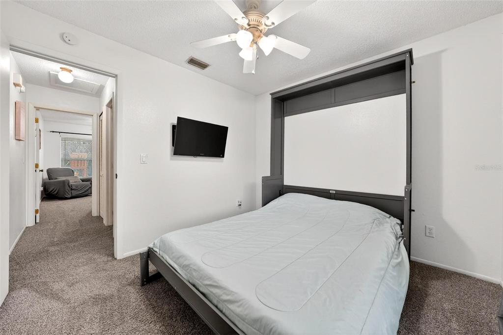 A bedroom features a gray Murphy bed, a wall-mounted television, and a ceiling fan — 5107 DEER CREEK DRIVE, ORLANDO, FL