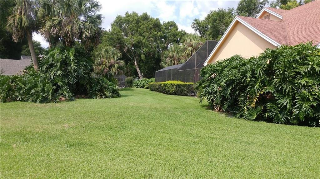 A grassy backyard features a large house with a screened-in pool enclosure and lush landscaping — 2630 STANTON HALL COURT, WINDERMERE, FL