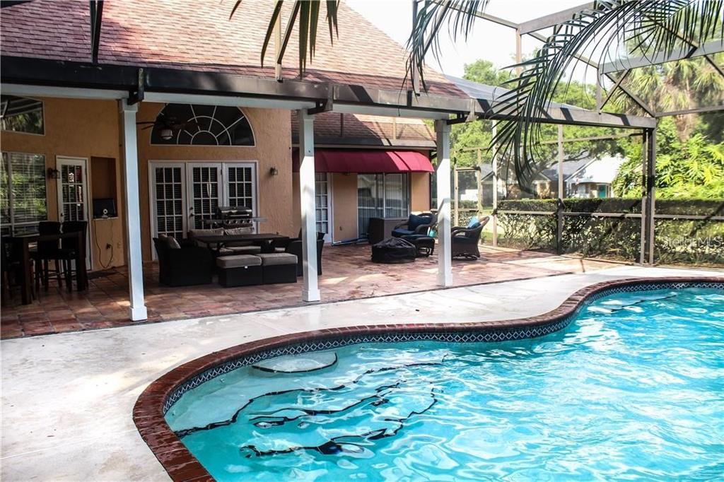 A swimming pool sits in front of a covered patio with outdoor furniture and seating — 2630 STANTON HALL COURT, WINDERMERE, FL