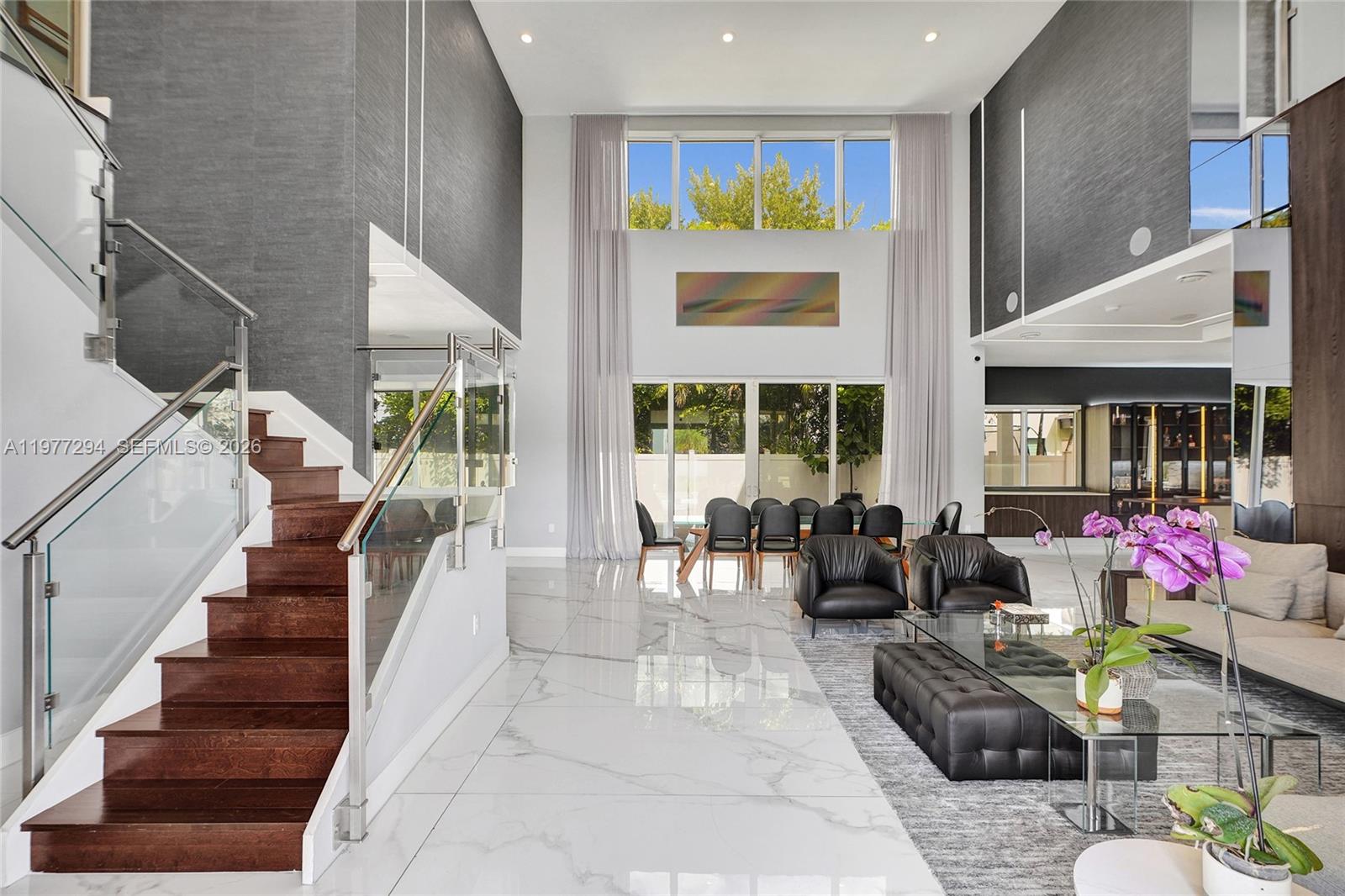 A modern, high-ceilinged living and dining area features white marble floors and a wooden staircase — 10223 NW 75th Ter, Doral FL 33178, DORAL, FL