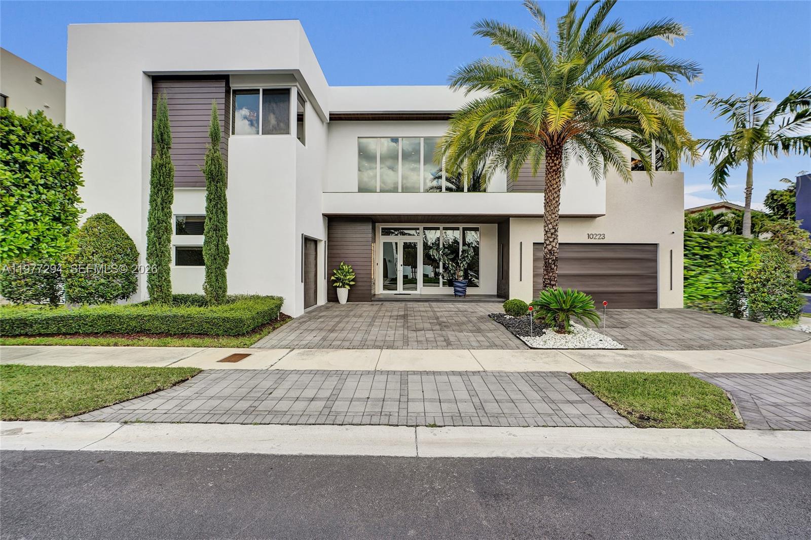 A modern two-story house features a white facade, dark wood accents, and a paved driveway — 10223 NW 75th Ter, Doral FL 33178, DORAL, FL