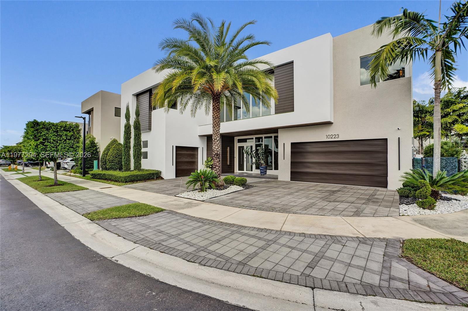 A modern two-story house features a paved driveway, a palm tree, and a double garage — 10223 NW 75th Ter, Doral FL 33178, DORAL, FL