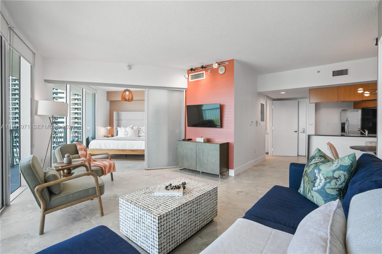 A modern living room with a blue sofa, tiled floors, and a sliding glass bedroom partition — 1750 N Bayshore Dr # 1401, Miami FL 33132, MIAMI, FL