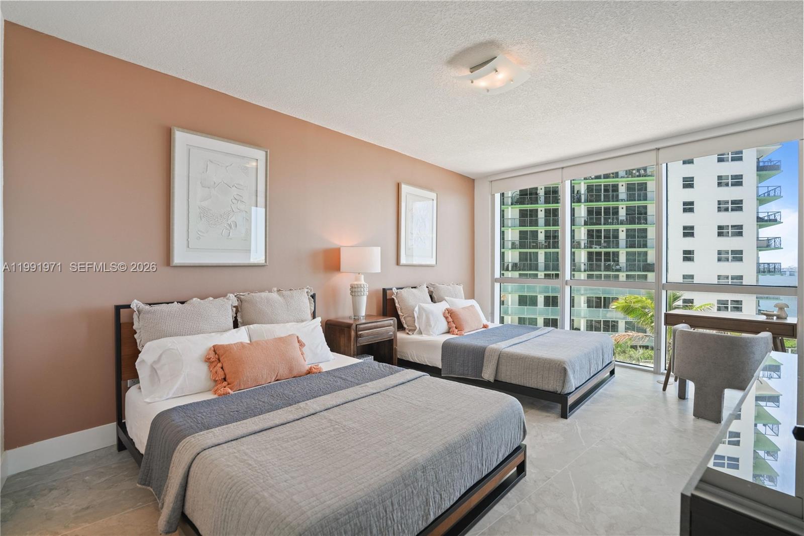 A bedroom with two beds, peach walls, and floor-to-ceiling windows overlooking a neighboring building — 1750 N Bayshore Dr # 1401, Miami FL 33132, MIAMI, FL
