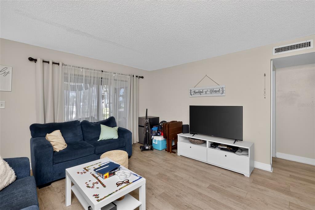 A living room with light wood-look flooring, a blue sofa, and a white media console — 2650 COUNTRYSIDE BOULEVARD UNIT B104, CLEARWATER, FL