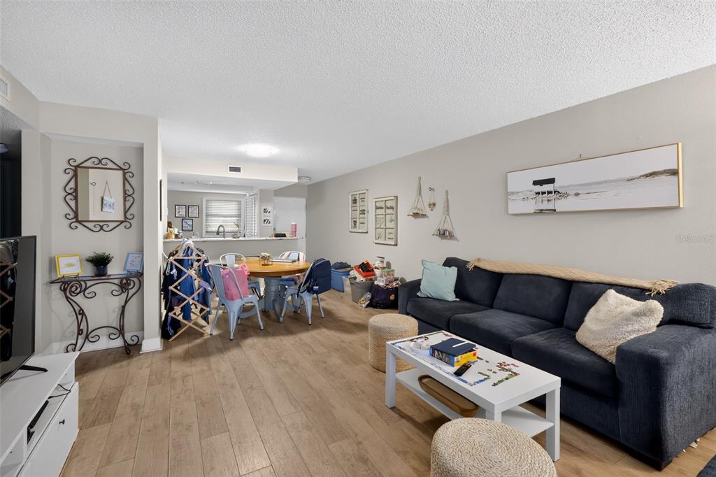 A living room with light wood flooring, a blue sofa, and an adjacent dining area — 2650 COUNTRYSIDE BOULEVARD UNIT B104, CLEARWATER, FL