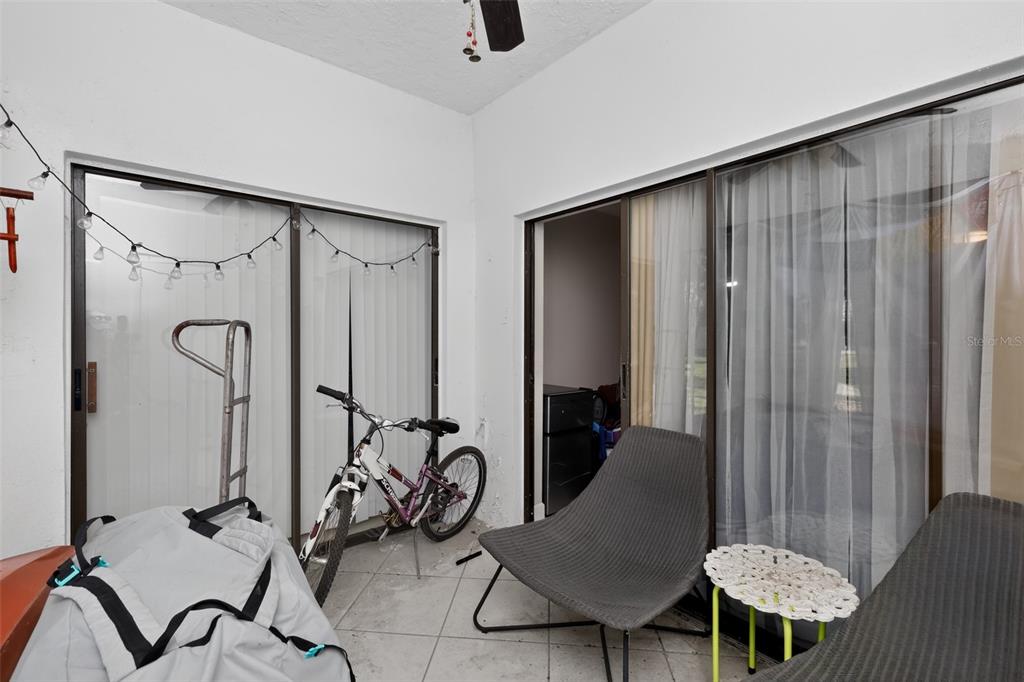 A covered patio features tiled flooring, sliding glass doors, a bicycle, and outdoor furniture — 2650 COUNTRYSIDE BOULEVARD UNIT B104, CLEARWATER, FL