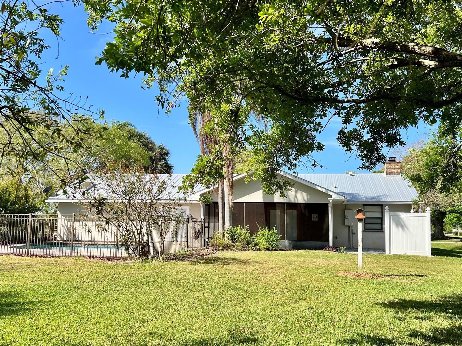 A backyard view of a single-story house with a metal roof, pool, and screened porch — 352 SW 85th Avenue, Okeechobee FL 34974, OKEECHOBEE, FL