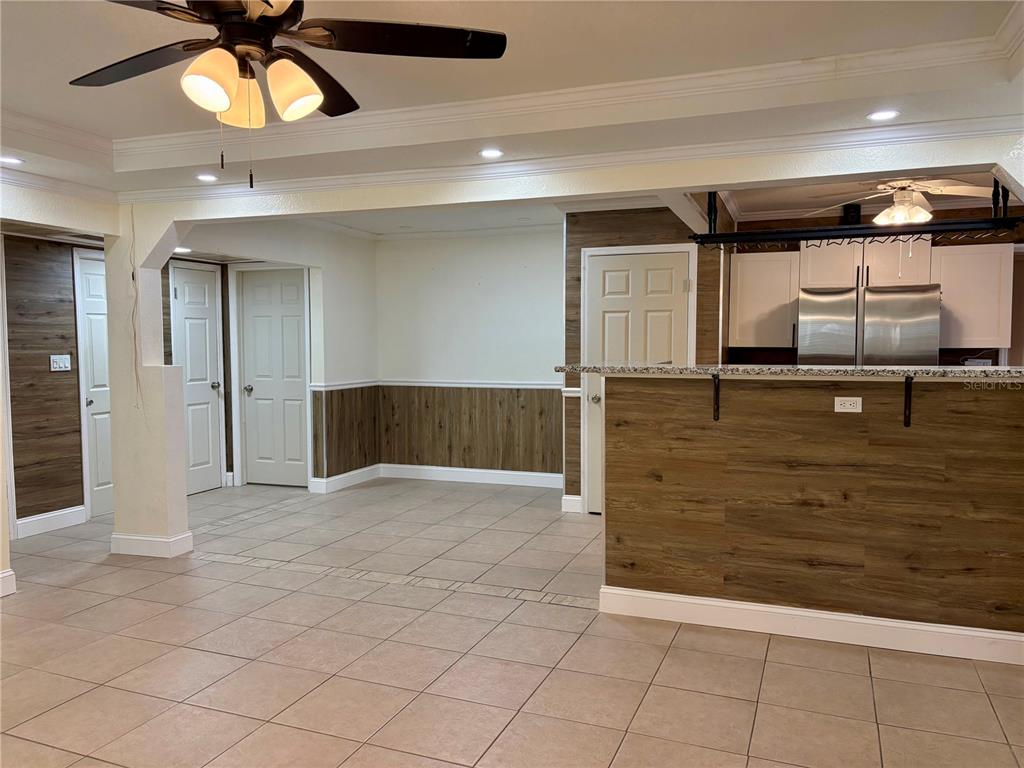 A room with tile flooring, wood-look wainscoting, a kitchen pass-through, and a ceiling fan — 1708 E MAIN STREET, LAKELAND, FL