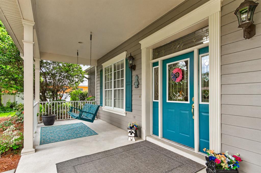 A covered front porch features a teal door, a hanging swing, and a gray rug — 6130 BRIDLEFORD DRIVE, WESLEY CHAPEL, FL
