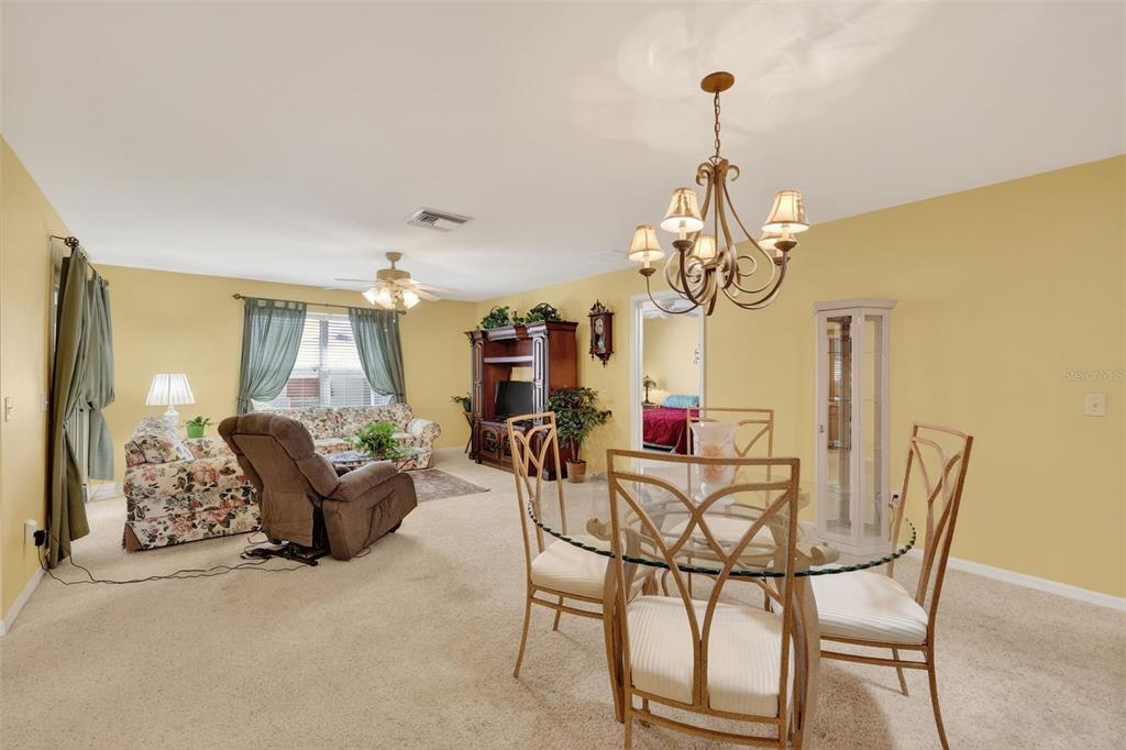 A living and dining area with yellow walls, beige carpeting, and a glass dining table — 17369 SE 75TH COACHMAN COURT, THE VILLAGES, FL