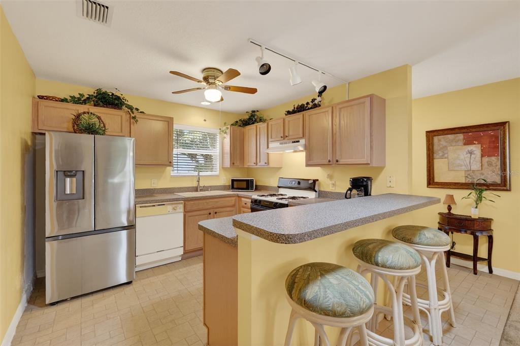 A kitchen with light wood cabinets, stainless steel appliances, and a breakfast bar with stools — 17369 SE 75TH COACHMAN COURT, THE VILLAGES, FL