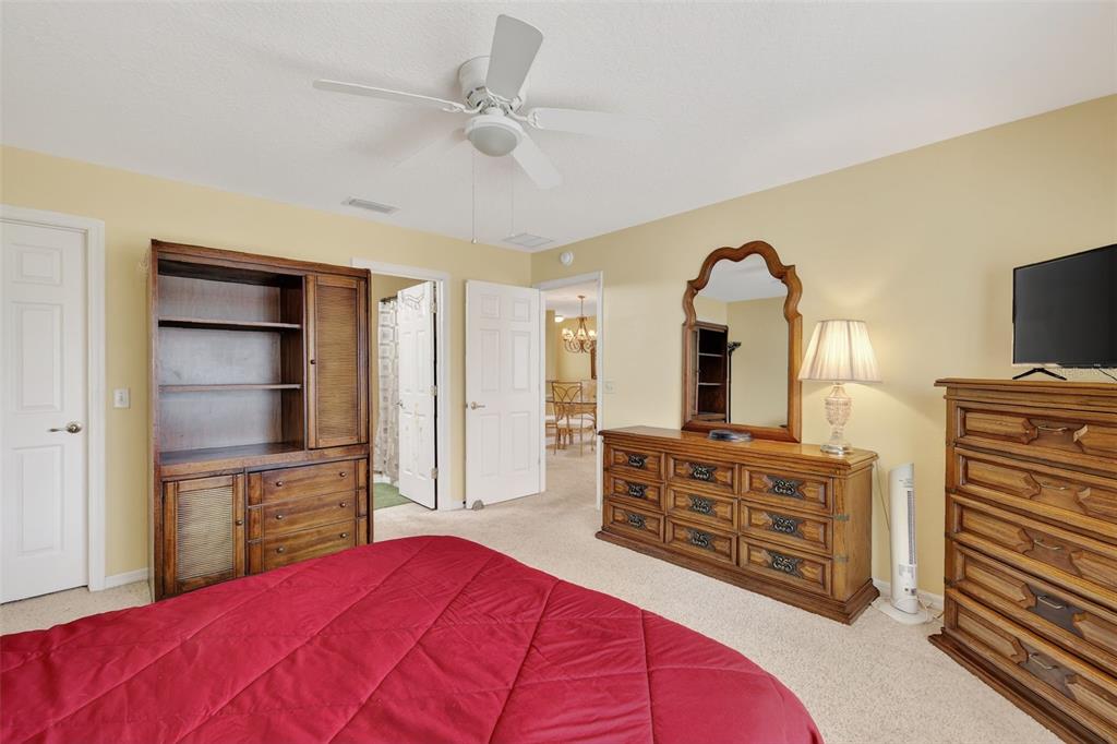 A bedroom features a red bedspread, wooden furniture, a ceiling fan, and beige carpet — 17369 SE 75TH COACHMAN COURT, THE VILLAGES, FL
