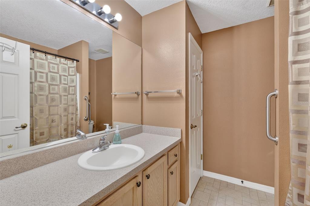 A bathroom features a light-colored vanity, a large mirror, and a shower with a curtain — 17369 SE 75TH COACHMAN COURT, THE VILLAGES, FL