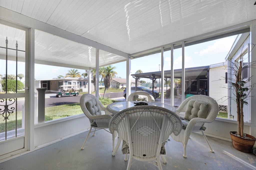 A screened-in patio features white wicker furniture, a glass-top table, and views of the neighborhood — 2100 KINGS HIGHWAY UNIT 877, PORT CHARLOTTE, FL