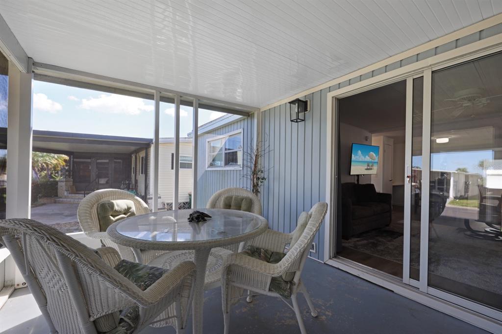 A covered patio features a glass-topped wicker table with chairs and sliding glass doors — 2100 KINGS HIGHWAY UNIT 877, PORT CHARLOTTE, FL