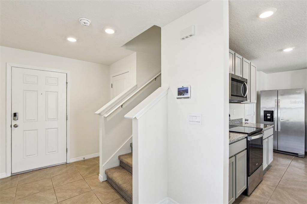 An entryway with tiled floors leads to a carpeted staircase next to a modern kitchen — 36557 NIGHT STRAWBERRY COURT, DADE CITY, FL
