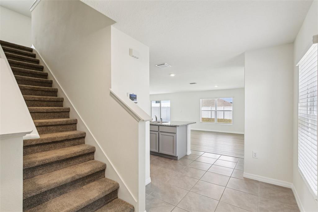 A carpeted staircase leads to an open-concept kitchen and living area with tile flooring — 36557 NIGHT STRAWBERRY COURT, DADE CITY, FL