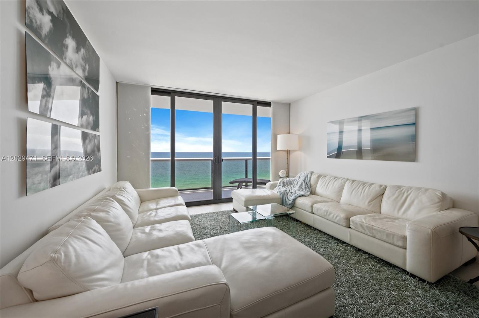 A living room features two white leather sectionals, a glass coffee table, and ocean views — 9455 Collins Ave # 1208, Surfside FL 33154, SURFSIDE, FL