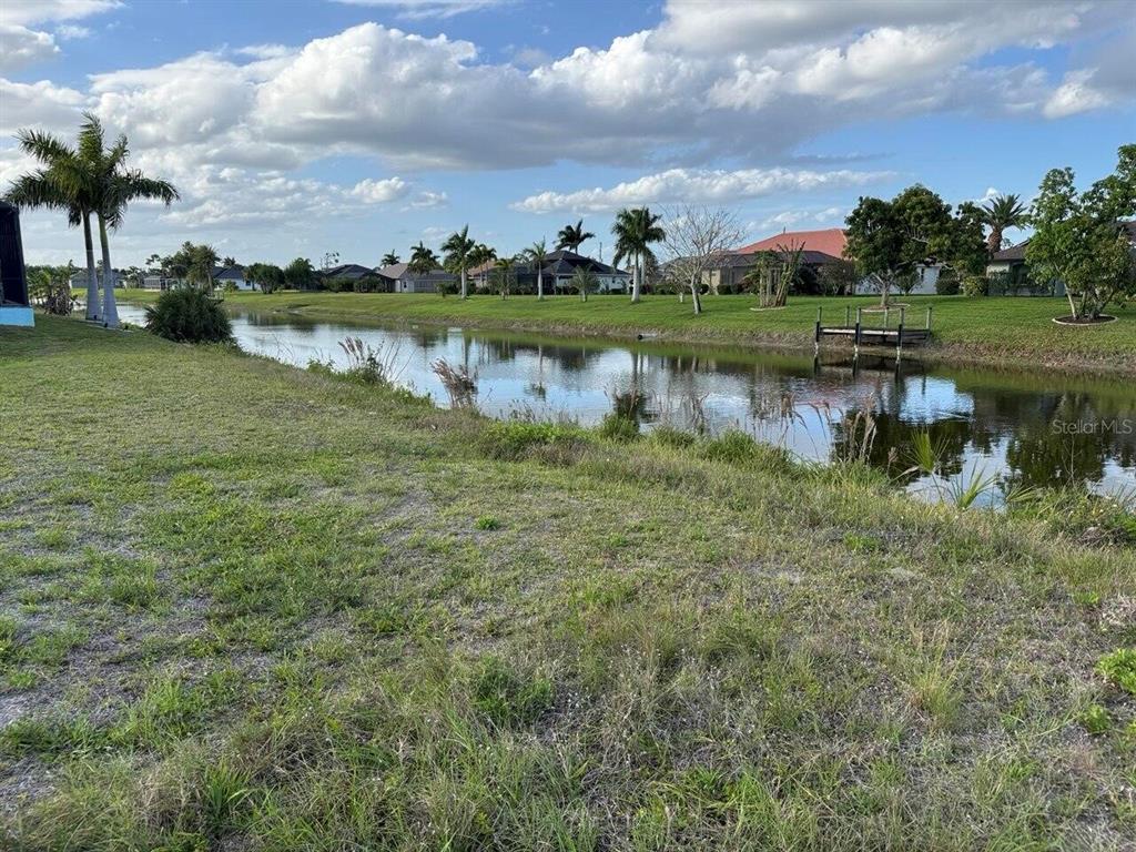 A grassy yard overlooks a narrow canal with a small wooden dock and palm trees — 743 ROTONDA CIRCLE, ROTONDA WEST, FL
