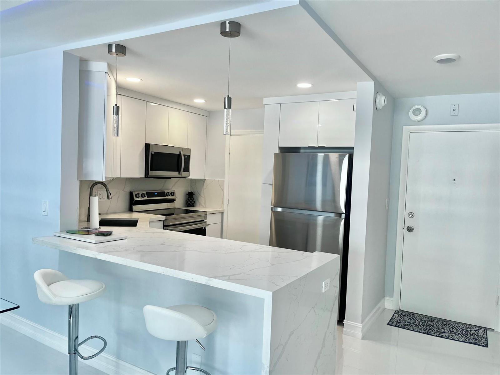 A modern kitchen features white cabinets, stainless steel appliances, and a marble-patterned waterfall island — 133 N Pompano Beach Boulevard # 105, Pompano Beach FL 33062, POMPANO BEACH, FL